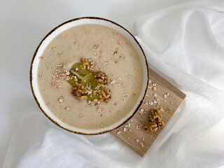 Creamy oatmeal porridge in a bowl on a wooden board on a white background. Healthy food with walnuts, kiwi, and oat flakes. Nutritious breakfast morning meal.