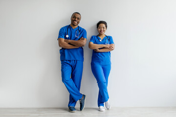 Portrait of two African American healthcare professionals in blue scrubs, confidently standing with...