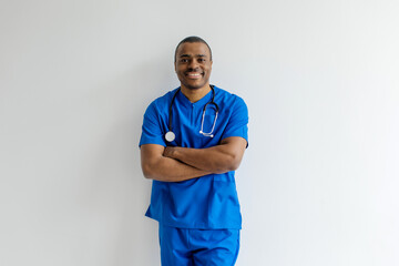 Portrait of a smiling African American male nurse or doctor in blue scrubs standing with arms...