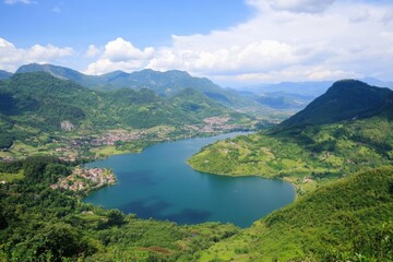 Obraz premium Scenic view of lake, hills, town, and mountains under a partly cloudy sky