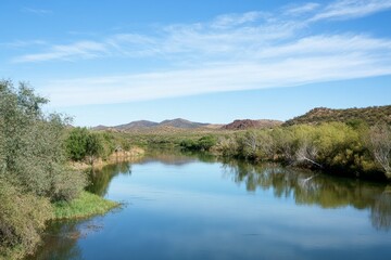 Fototapeta premium Serene river flows through arid landscape under a bright, blue sky