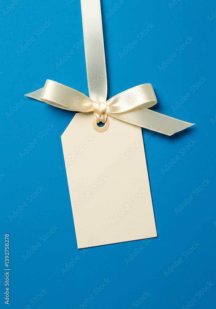 Aufkleber blank tag with ribbon on blue. tag is cream color. the ribbon is tied in a bow. simple tag for messa