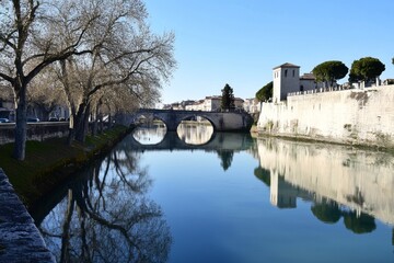 Obraz premium Tranquil river reflects arch bridge, trees, and fortified embankment