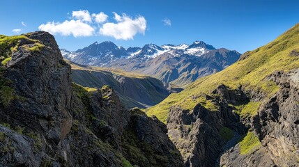 Obraz premium Majestic snow-capped mountains overlook a rugged, verdant valley under a bright blue sky