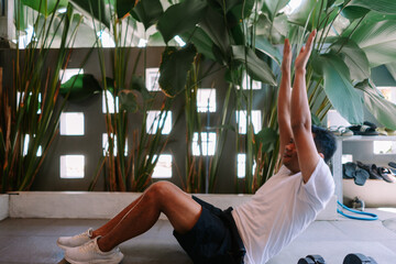 Fototapeta premium Man doing crunches at his home gym with tropical plant background