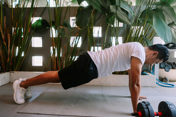 Man doing push-ups outdoors surrounded by tropical greenery and weights