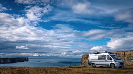 Scenic view of a camper van parked by the cliffs overlooking the ocean under a cloudy sky