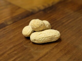 A small pile of unshelled peanuts rests on a wooden table, showcasing natural texture and earthy tones.