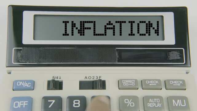 "Inflation" text or words displayed on a calculator's LED screen as a hand types numbers, symbolizing the economic concept of rising prices and reduced purchasing power over time