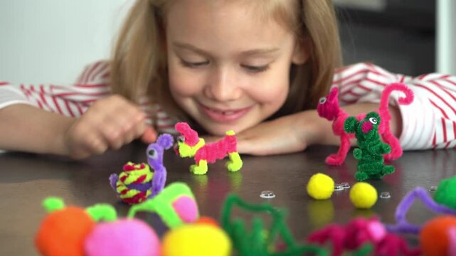 Portrait of little girl fun make diy from colored chenille wire and plays with toy dog. Creation handmade craft. Children leisure