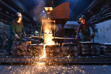 Group of workers in an iron foundry - casting a workpiece with liquid hot metal into a mold - cooperation and work safety