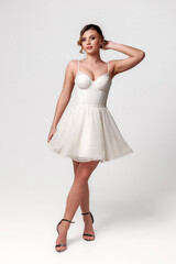 Naklejka premium Young woman in elegant white dress poses confidently in a studio setting with minimalistic background