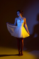 Elegant woman poses in sparkling white dress under colorful lights during a creative studio...
