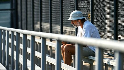 A tennis fan checks scores on a phone in a calm morning bleacher - Powered by Adobe