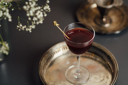 Close up of a red cocktail in a stylish glass placed on a decorative metallic tray, complemented by delicate table decor, creating a sophisticated ambiance