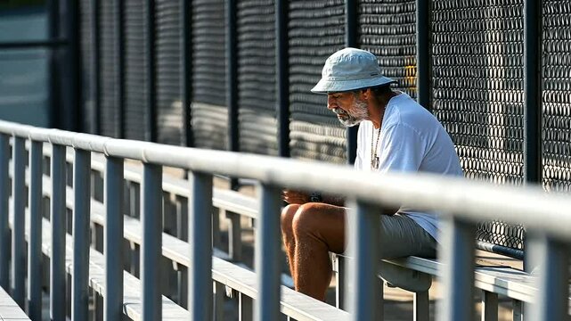 A tennis fan checks scores on a phone in a calm morning bleacher