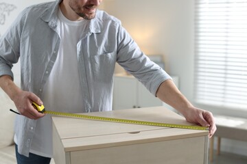 Man measuring wooden cabinet with tape indoors, closeup