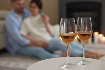 Couple near fireplace at home, focus on glasses of wine