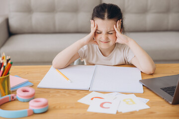 Naklejka premium Remote Study Stress. Sad Little Girl Sitting At Desk With Laptop, Upset Female Child Making Facepalm Gesture, Tired Of Distance