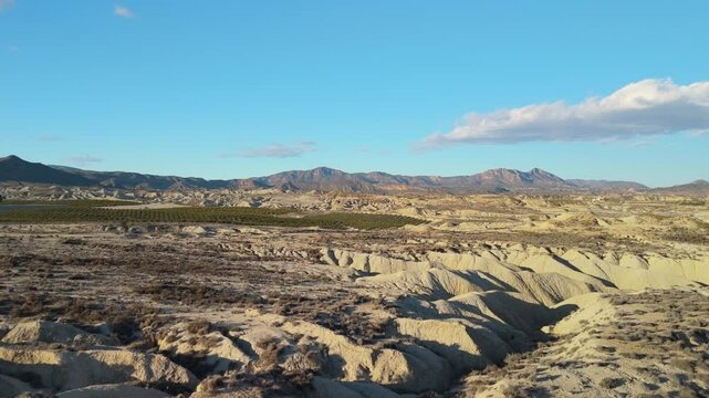 Wide aerial view unveiling the geological formations of the tabernas desert, a unique landscape in spain, under a vast blue sky with sparse clouds