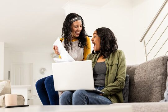 Celebrating success, diverse female friends using laptop at home, smiling joyfully - Powered by Adobe