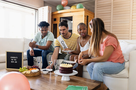 Celebrating new job, diverse friends enjoying cake and drinks in living room, at home