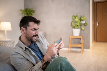 Frustrated man losing while playing videogames on mobile phone at home