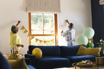 Celebrating birthday, decorating living room with banners and balloons, senior couple together