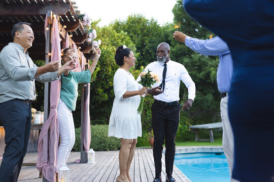 At wedding, Celebrating by poolside, senior couple with friends holding sparklers, smiling joyfully