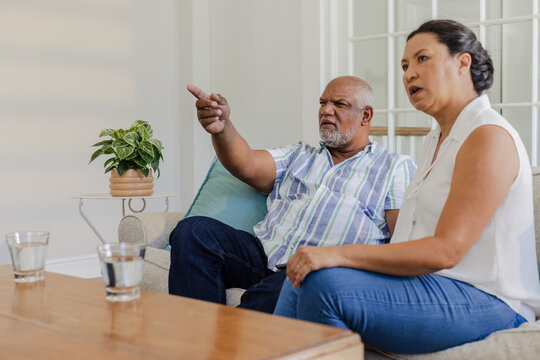 Senior couple sitting on couch, discussing and pointing at something in living room