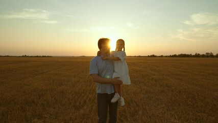 Father holding kid in arms in field at sunset. Happy cheery parent child kid strolling moving going across huge yellow meadow. Girl sits in man arms pointing with finger. Love fatherhood parenthood