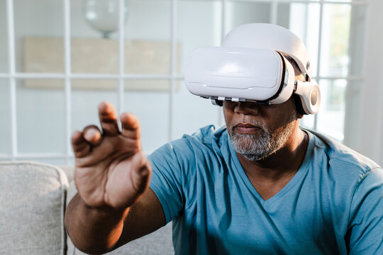 Senior African American man using VR headset at home, exploring virtual reality experience