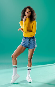 Confident woman in yellow top and denim shorts posing against green backdrop