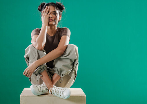 Young woman sitting on box covering face, expressing emotion in grunge style