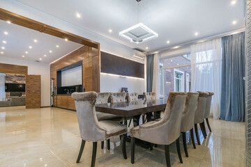 The interior of an open-plan country house. A dining table with upholstered chairs and a wide passage to the kitchen and living room.