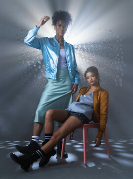 Standing confidently, African American woman while another woman sits relaxed on chair