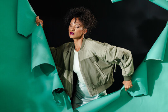 Breaking through green paper wall, African American woman showing determination