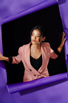 Woman in stylish pink blazer posing confidently against torn purple paper backdrop