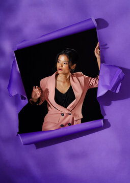 Asian woman in stylish pink blazer posing confidently through torn purple paper