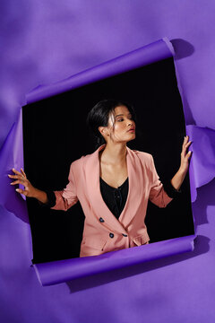 Asian woman in pink blazer posing confidently against torn purple paper backdrop