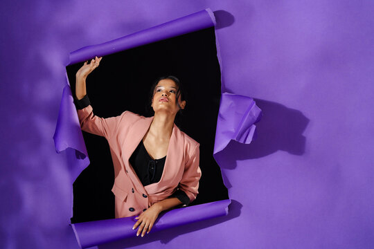 Breaking through purple paper wall, woman in pink blazer expressing freedom