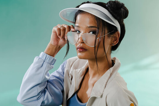 Stylish woman adjusting sunglasses wearing visor and jacket, exuding cool confidence