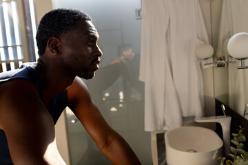 Contemplative African American man in bathroom leaning on sink, reflecting in morning light