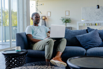 African American African American man using laptop on sofa at home, working remotely