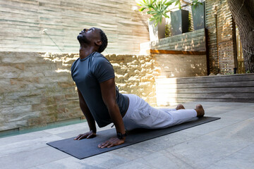 African American man practicing yoga on mat by pool, enjoying morning exercise