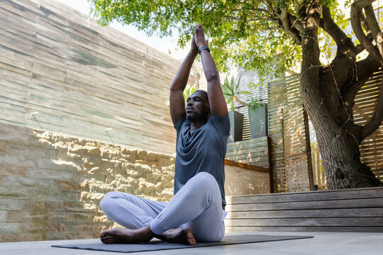 African American African American man practicing yoga outdoors, meditating on mat under tree - Powered by Adobe