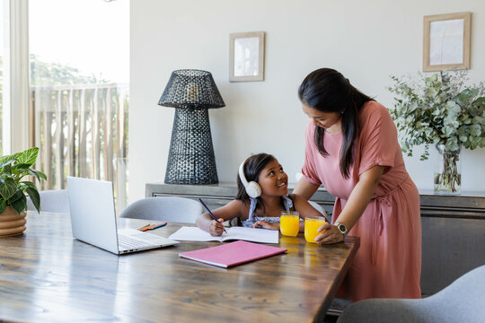 Mother helping daughter with homework at home, both smiling and enjoying time