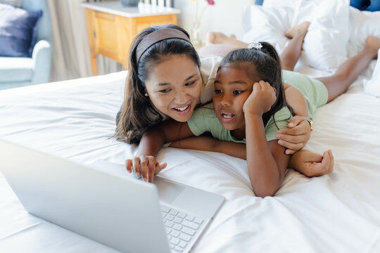 Mother and daughter watching laptop together on bed, enjoying quality time