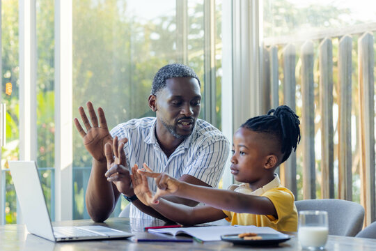 African American father teaching son math using laptop at home, bonding and learning together
