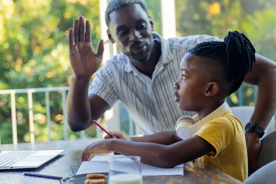 Father and son studying together at home, using laptop and taking notes
